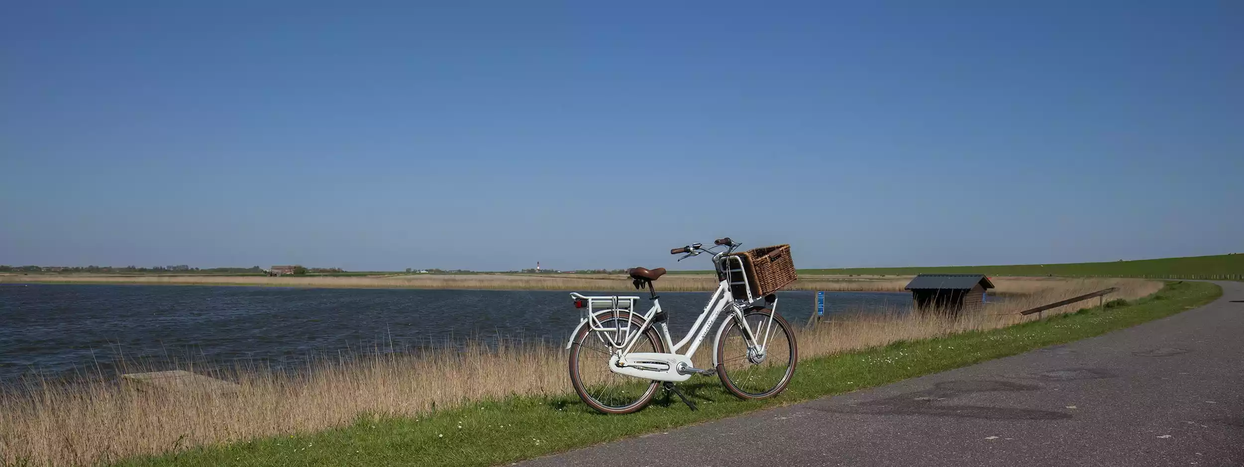 Weißes Fahrrad mit Korb am Radweg vor dem See