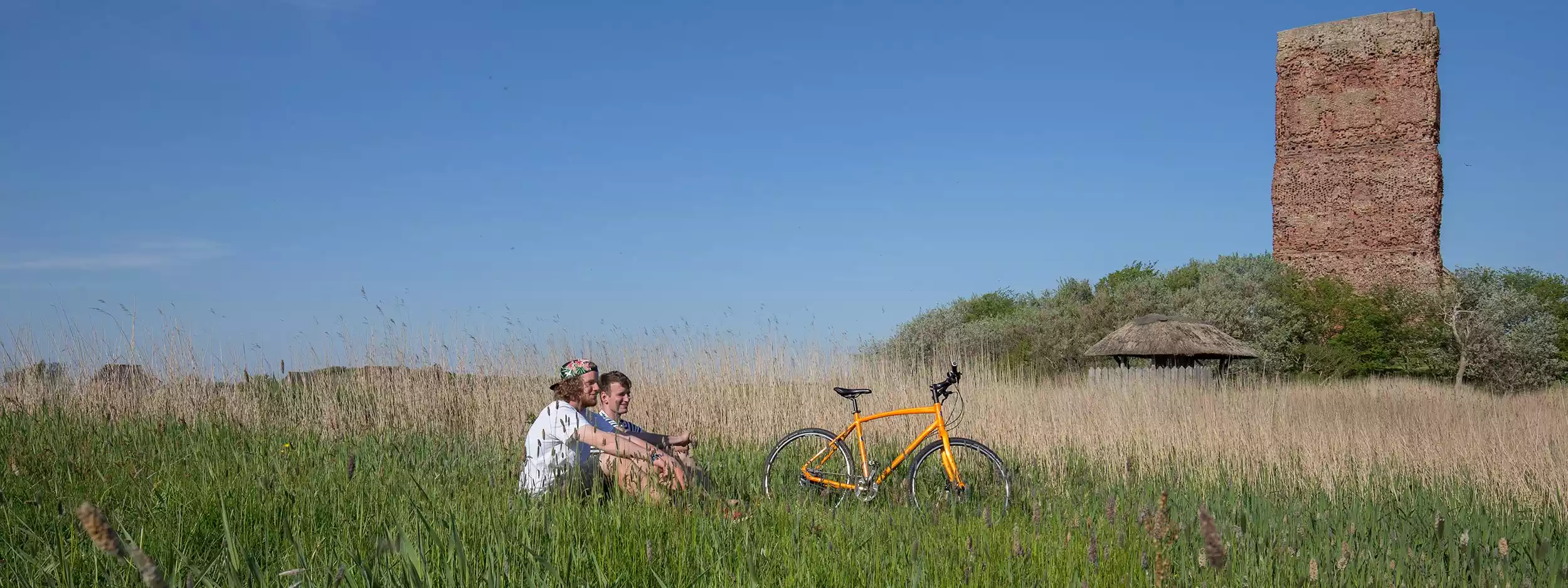 Paar sitzt im Gras neben Fahrrad an einer Ruine