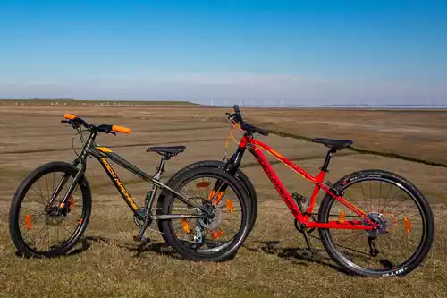 Zwei sportliche Kinderfahrräder auf Pellworm – schwarz-orange und rot vor Marschlandschaft